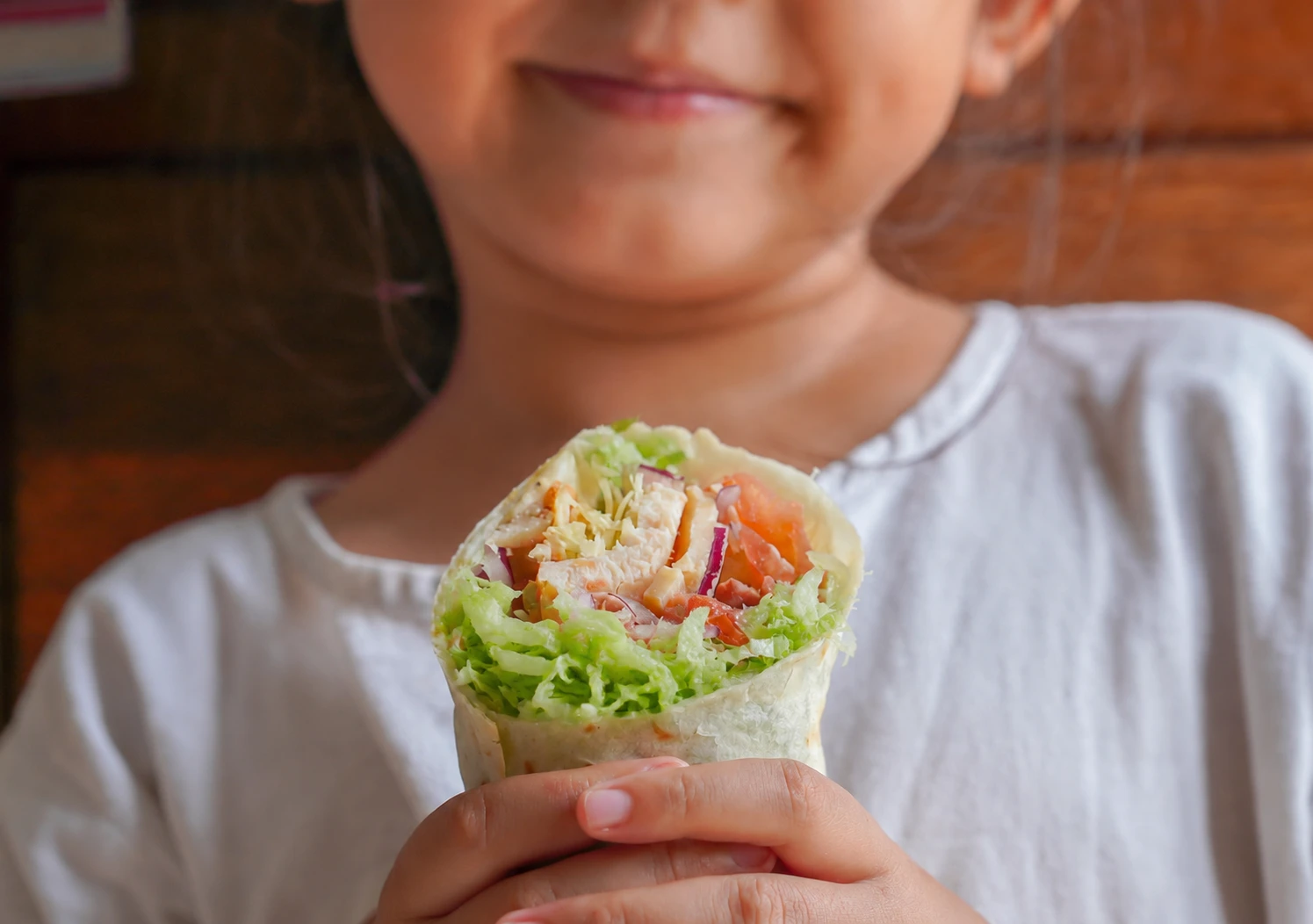 Criança segurando wrap de frango com acelga fresca, uma opção prática e saudável para o lanche.